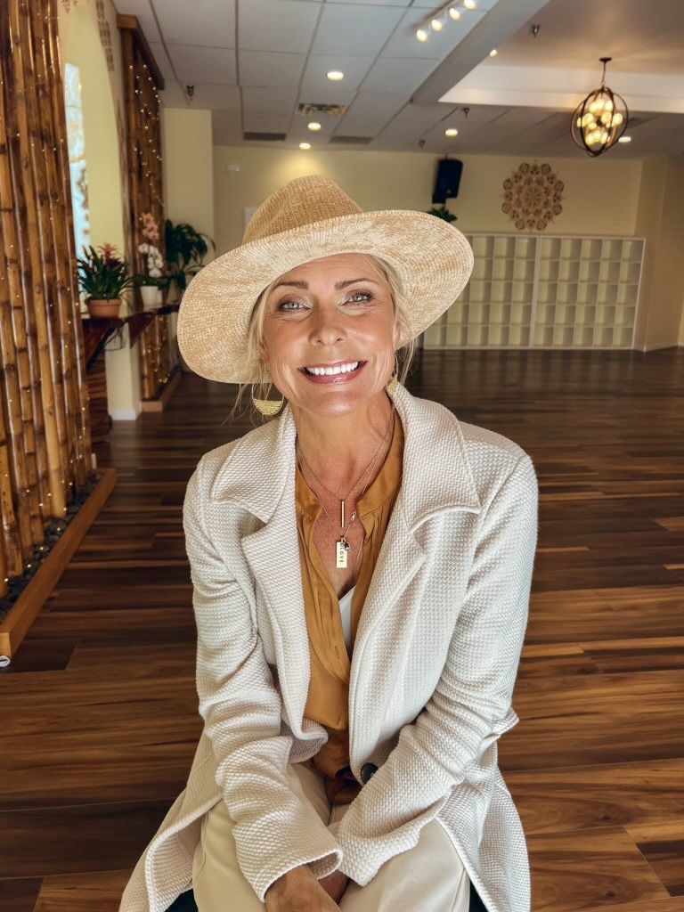 Eva Maurice seated in a retreat room, wearing a straw hat and cream jacket, laughing
